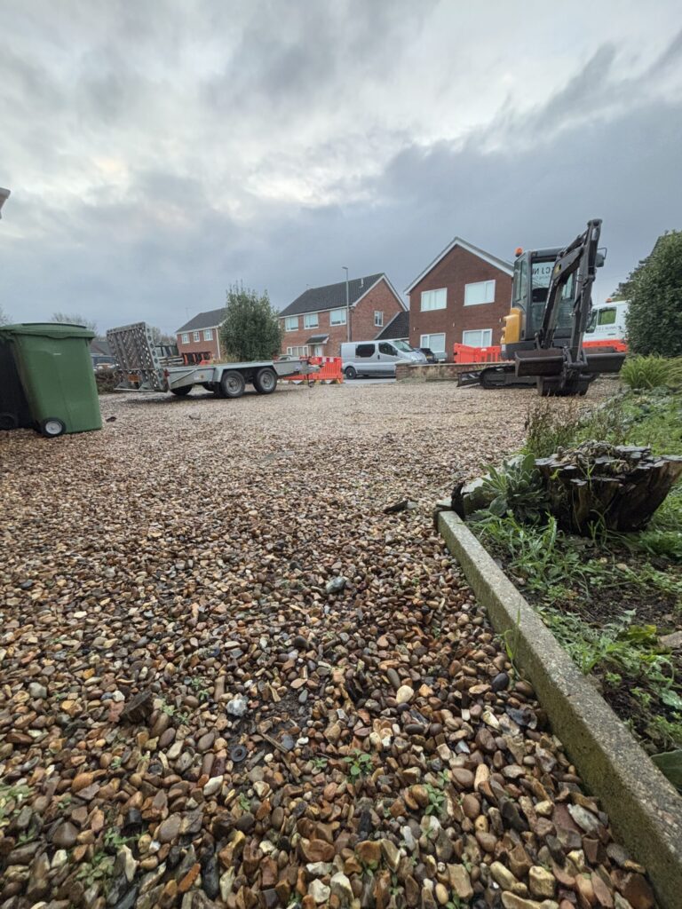 digger on a shingle driveway with a trailer and lorry in the background excavating