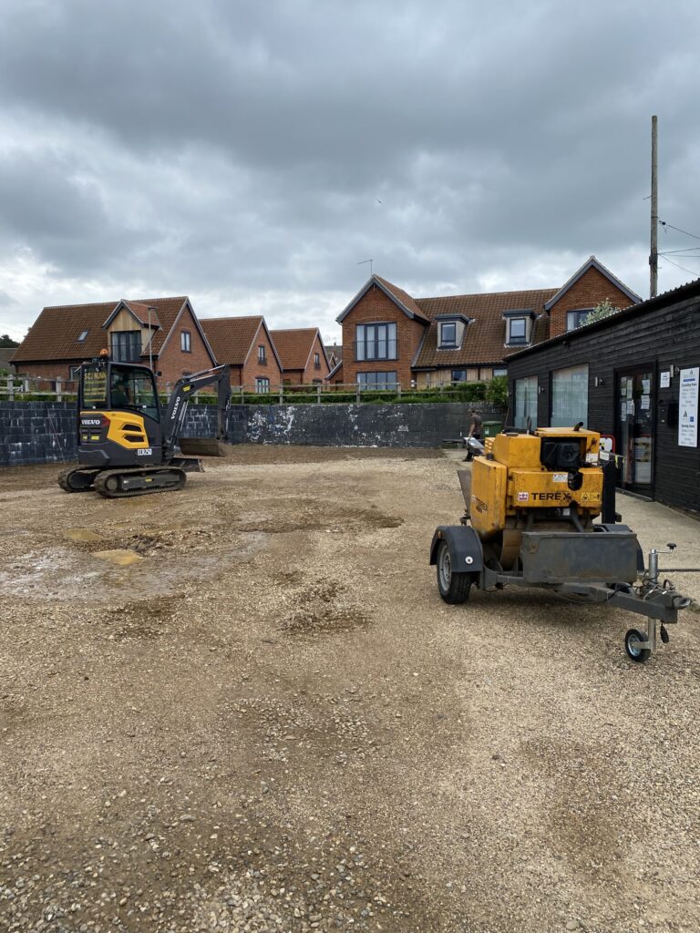 Excavator and tarmac roller on construction site with houses in background doing groundworks