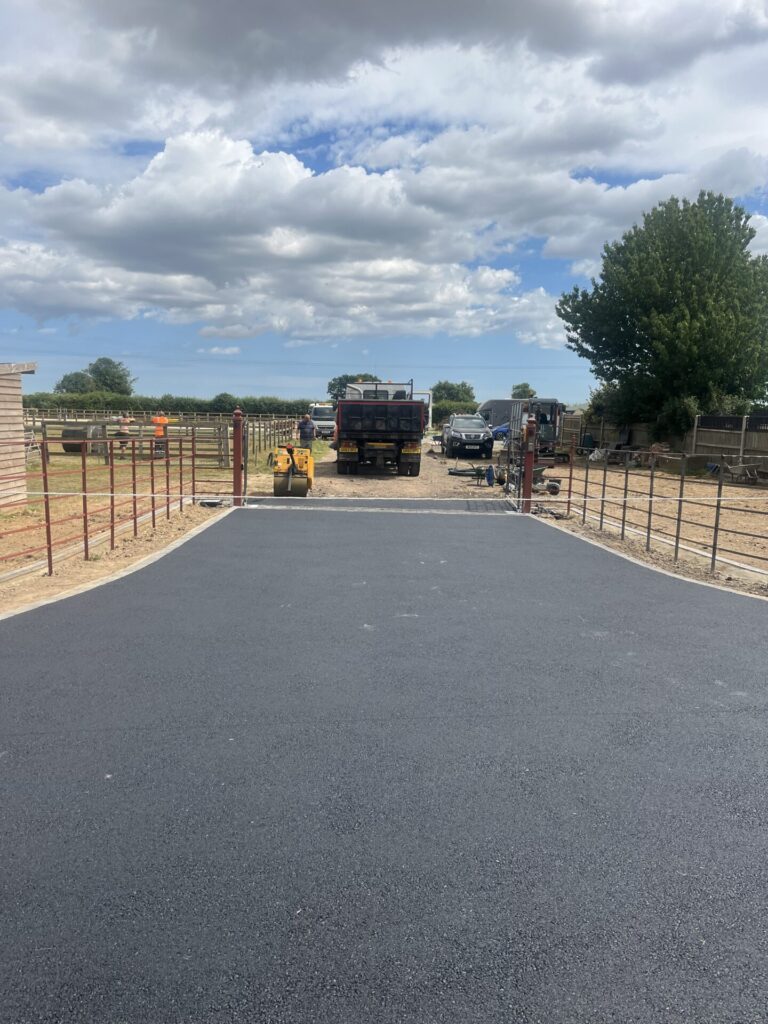Tarmac road entrance to farm in norfolk edged with concrete edging blocks with tarmac lorry and asphalt roller